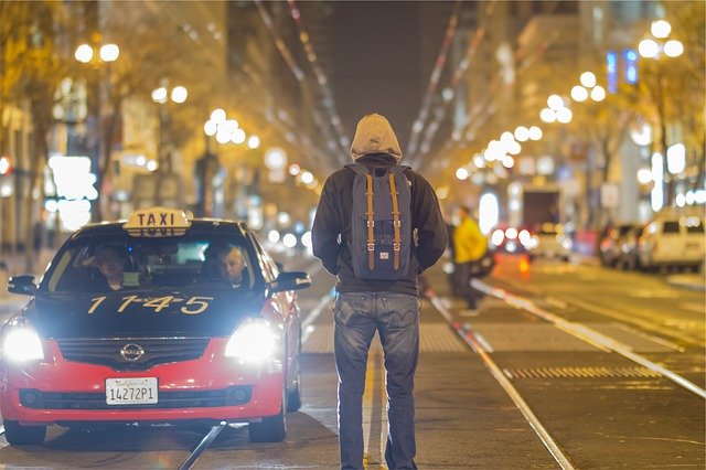 Taxi zastavující pocestnému s batohem na ulici
